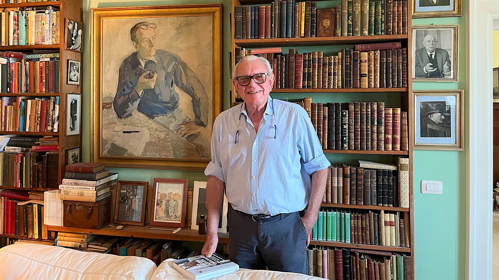  Peter Vinding-Diers stands in his library in front of shelves of books and a portrait of his father